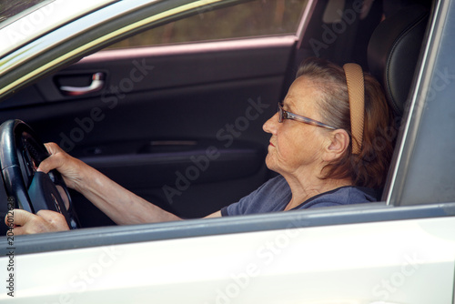 Old woman driving a car in the countryside, road trip concept.  Portrait of an old woman driving and near a car, on a walk outside the city.