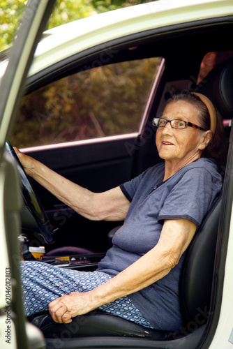 Old woman driving a car in the countryside, road trip concept.  Portrait of an old woman driving and near a car, on a walk outside the city.