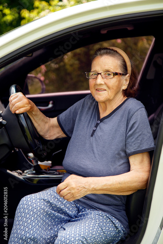Old woman driving a car in the countryside, road trip concept.  Portrait of an old woman driving and near a car, on a walk outside the city.