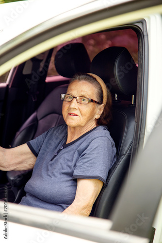 Old woman driving a car in the countryside, road trip concept.  Portrait of an old woman driving and near a car, on a walk outside the city.