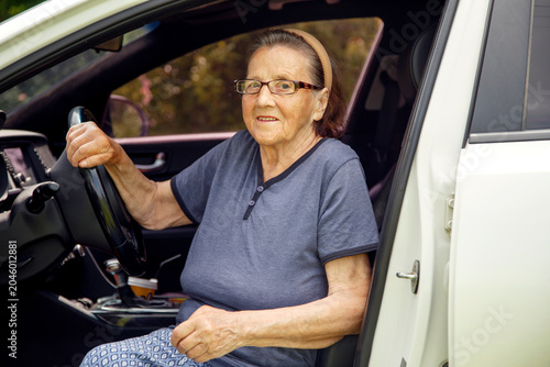 Old woman driving a car in the countryside, road trip concept.  Portrait of an old woman driving and near a car, on a walk outside the city.