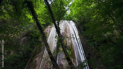 Tall Forest Waterfall Cascading Down Rocky Cliff in Natural Wilderness