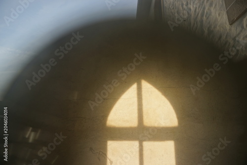 Abstraktes Motiv mit Kirchenfassade und Spiegelung von braunem Rundbogenfenster mit goldgelbem Licht bei Sonne am Abend im Sommer