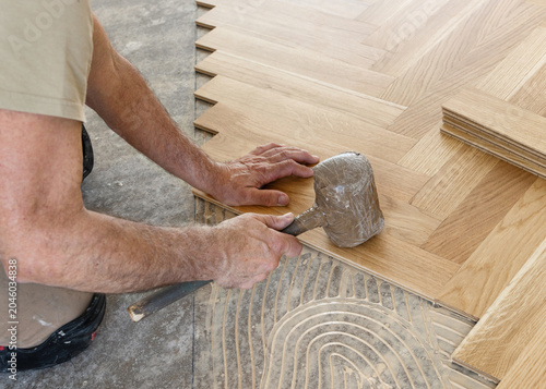 Worker installing herringbone parquet flooring with rubber mallet during hardwood floor installation