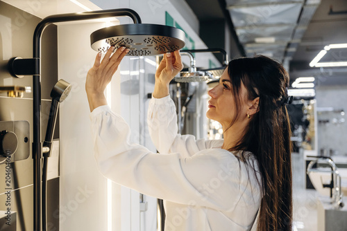 Bild auf Leinwand Female interior designer inspects modern showerhead fixture in a contemporary ba