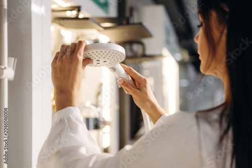 Foto Female customer inspecting modern showerhead in a home improvement store, surrou