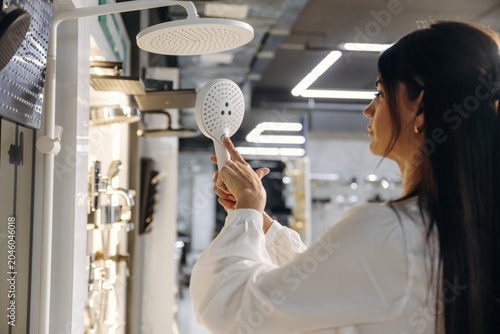 Tableau sur toile Woman examining modern showerhead design in a bathroom fixtures showroom, variou