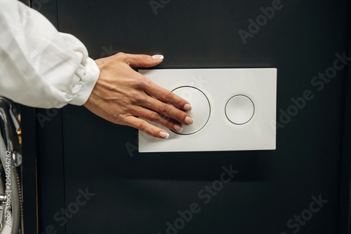 Fotografie Hand of a person with manicured nails pressing a modern dual flush toilet button