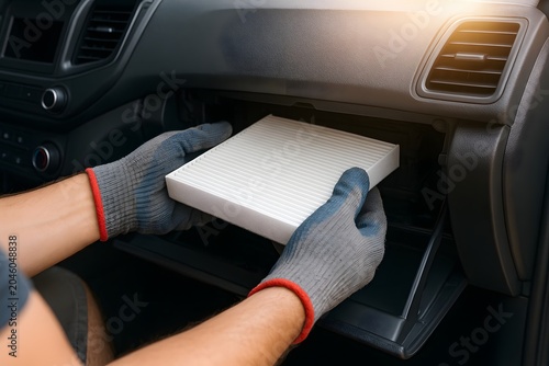 Close-up of hands wearing gray gloves, replacing a white car cabin air filter inside a car's glove compartment.