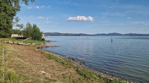 Scenic view of Lake Trasimeno shore with calm water under a blue sky in Umbria, Italy