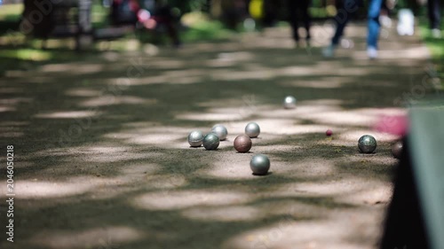 People play petanque in a park on a sunny day with trees and shadows in the background