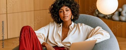 Confident woman working on laptop while relaxed in a modern gray lounge chair at home