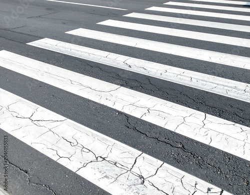 Close-up of asphalt road and crosswalk stripes. The white paint is cracking in certain areas, adding texture to the surface