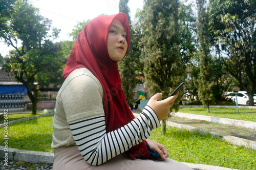 Young Woman In Hijab Standing At Park And Looking Away While Holding Phones