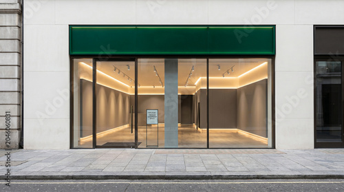 Empty commercial retail unit with dark green awning and large real estate shop front glass front recessed lighting store window store interio