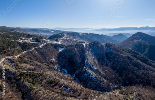 Aerial view of a vast mountain range under a clear blue sky, showcasing rugged terrain and sparse winter snow
