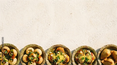 Top view of traditional indian street food snacks like pani puri, chaat, and samosa served in dried leaf bowls on a textured surface
