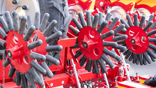 Fotografia Close up view of red farm machinery with multiple rotating rubber tine wheels, metal frame details, and mechanical parts