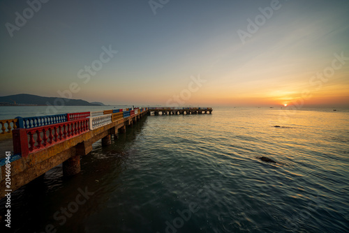 Foto Sun rising over the East Sea beside a colorful pier, creating a peaceful coastal morning scene