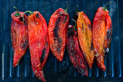 Salted and oiled red romano peppers ready grilled on a black sheet on a gas grill being grilled for a vegetarian meal. The scene captures healthy, vegan outdoor cooking during a bright summer day.