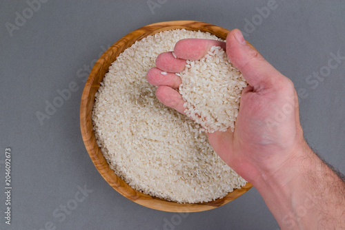 Fotografie Mano de hombre mostrando granos de arroz de un cuenco de madera lleno sobre fond