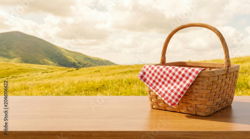 Empty picnic basket blanket layout over wooden table with sunny meadow and hill view background. summer leisure park. background fabric display, material textile nature, simple design surface