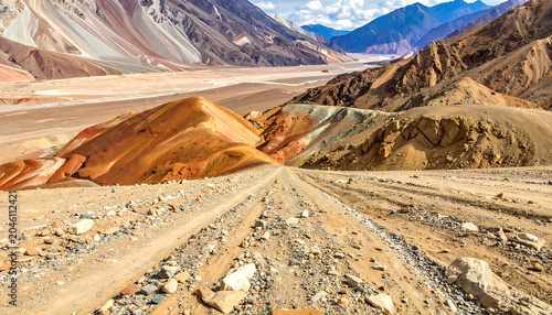 Dusty dirt road winding through colorful arid mountains under a clear sky, remote landscape, adventure journey concept