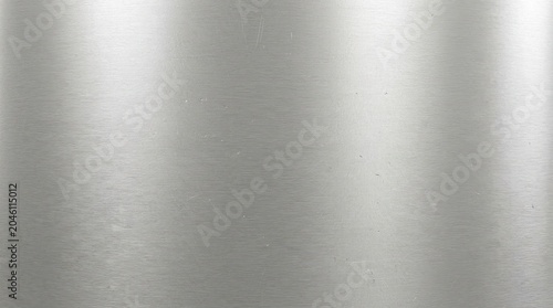 A smooth, reflective stainless steel surface is presented. The metal exhibits a gradient of light, transitioning from darker at the top to lighter at the bottom, creating a subtle sheen.