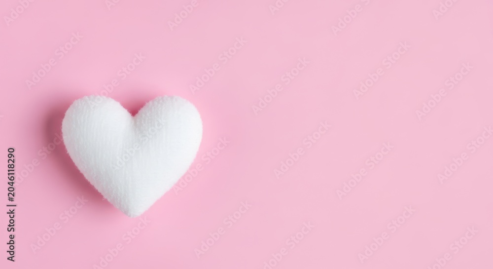 Fototapeta premium A soft white plush heart shape on a solid pastel pink background