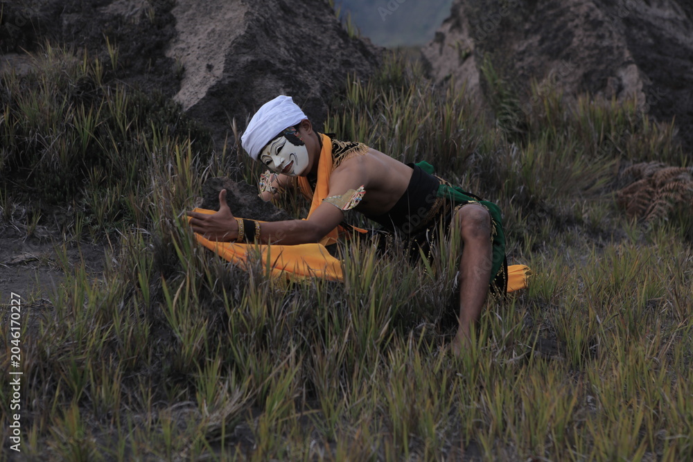 Fototapeta premium Traditional Javanese masked dancer posing in a grassy mountain field.
