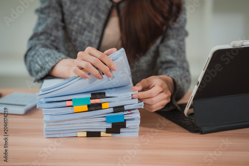Fotografie A close-up image of a businesswoman's hands rummaging through a large stack of documents on her desk, organizing papers and files in her office using a digital tablet