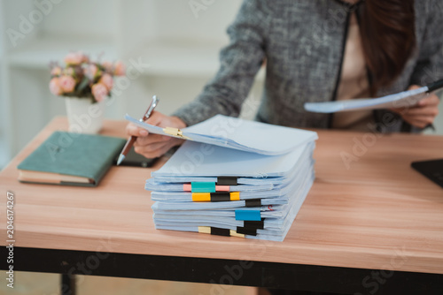 Fotografie A close-up image of a businesswoman's hands rummaging through a large stack of documents on her desk, organizing papers and files in her office using a digital tablet