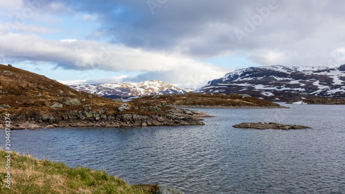 Remote mountain water resources on Haukeli plateau with alpine reservoir, rocky shoreline and snow covered highlands in Norway for hydrology, environment and climate related concepts