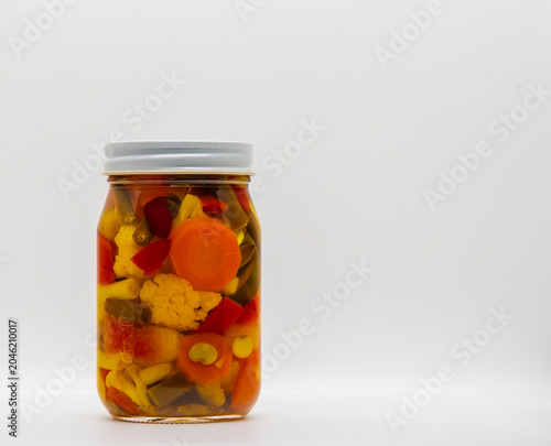 Fotografia A jar sits on a plain surface filled with a variety of mixed vegetables, called Chow Chow