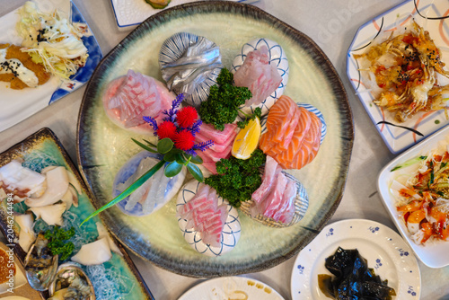 Assorted fresh sashimi platter with salmon and white fish beautifully presented on decorative dishes, premium seafood cuisine served with elegant garnish and side dishes.