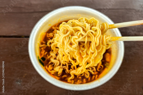Hot spicy instant cup noodles with chopsticks in a disposable bowl and steaming red broth ready to eat, showcasing popular Korean convenience food and quick meal culture.