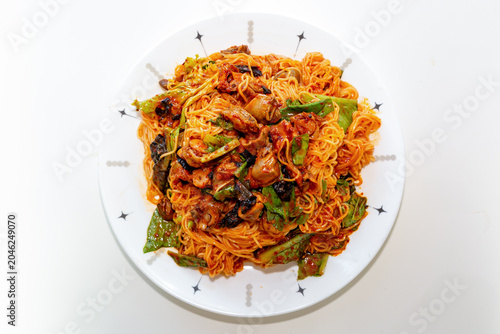 Spicy golbaengi somyeon with seasoned sea snails, fresh vegetables, and thin wheat noodles mixed in a savory Korean red pepper sauce on a white plate.