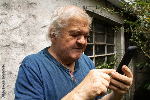 Primer plano de un hombre adulto mayor de 70 años concentrado usando un teléfono inteligente, escribiendo un mensaje o usando una aplicación en casa