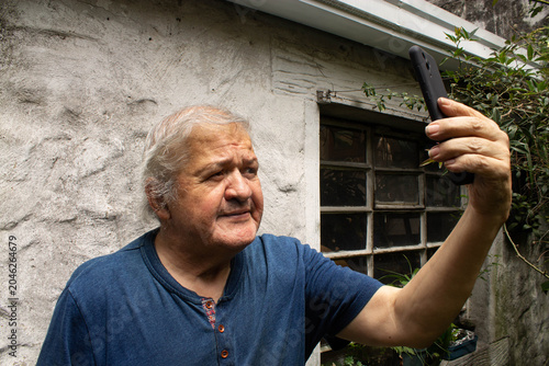 Billede på lærred Retrato de un hombre mayor sosteniendo un teléfono inteligente para tomarse una selfie o realizar una videollamada