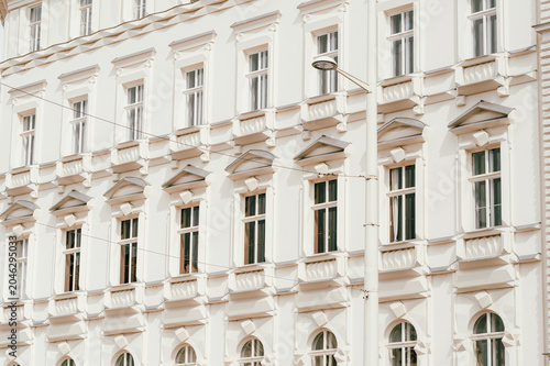 Close-framed view of a pale cream classical building facade featuring repeated windows, decorative cornices, pilasters, and balustrade-like ledges. Soft