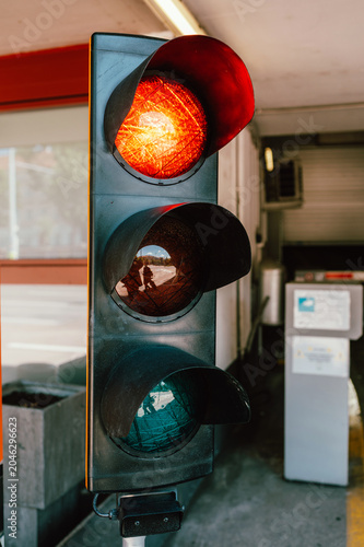 Vertical close-up of a three-lens traffic signal showing the top red light illuminated. The metal housing and visors are visible, with reflections in the