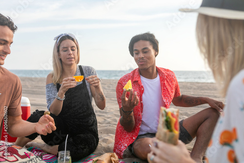 Photos Group of friends enjoying a picnic on the beach, sharing food.