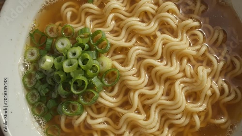 A bowl of hot instant ramen noodles with chopped green onions on a rustic wooden table