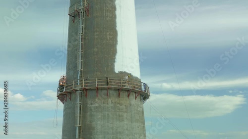 Industrial Painters Coating Tall Chimney Stack at Industrial Facility – Maintenance and Restoration Work at Height.Professional industrial painters performing maintenance and protective coating work