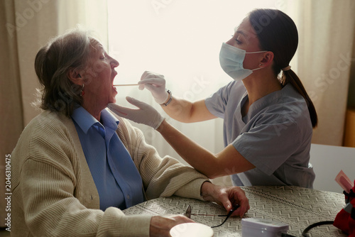 Slika na platnu Senior woman receiving throat swab examination from young adult female caregiver at home, supporting elder care and home healthcare
