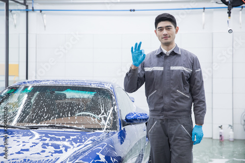 Fotografía Confident car wash worker with soapy blue car giving approval gesture