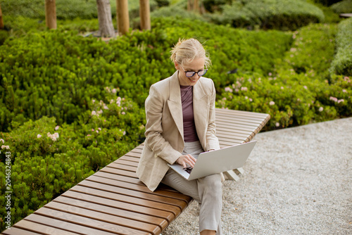 Billede på lærred Woman works on laptop in park surrounded by green plants and flowers in daytime