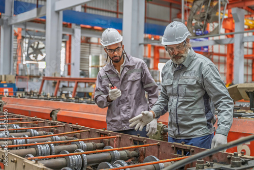 Two industrial workers inspecting machinery in a factory. Teamwork, precision, and safety gear highlight professional collaboration in metal production and mechanical maintenance.