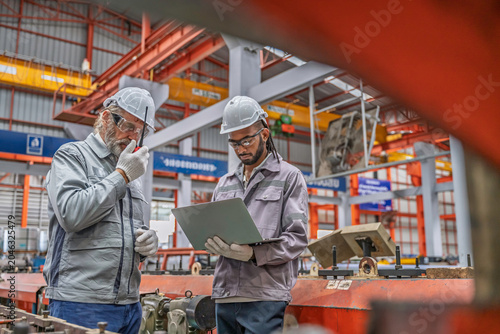 Two industrial workers inspecting machinery in a factory. Teamwork, precision, and safety gear highlight professional collaboration in metal production and mechanical maintenance.