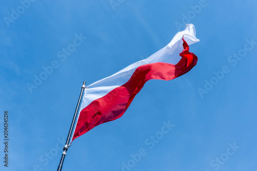 Polish national flag with red and white stripes waving proudly in strong wind against clear blue sky on a sunny day. Concept of national pride, independence, patriotism and state symbolism